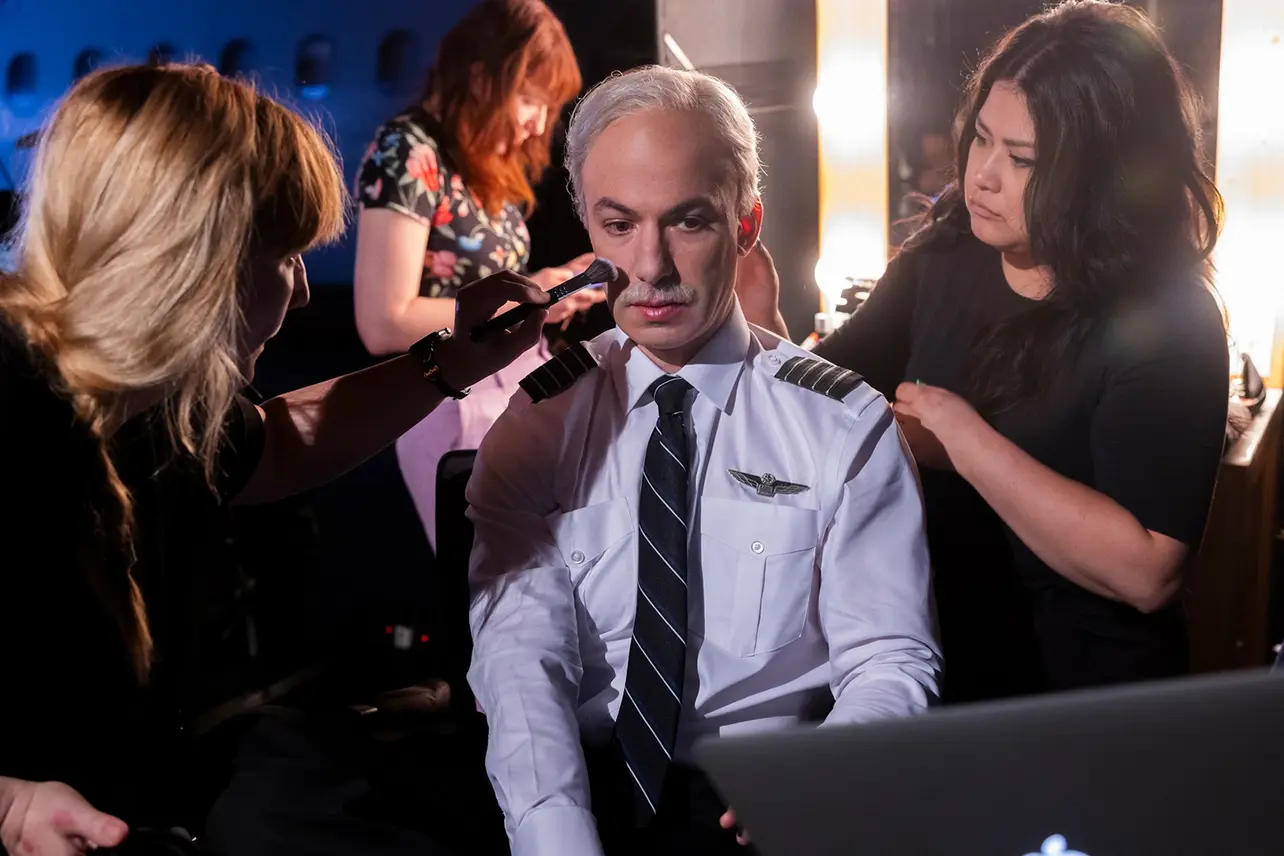 Nathan Fielder in a pilot uniform being prepared by wardrobe staff, a scene from The Rehearsal